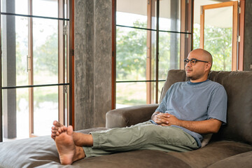 Handsome asian man sitting rest on sofa couch in living room at home. Happy Portrait of cheerful smiling asian man relax in the house. People quality time and successful in life