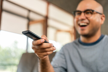 Young asian man watching television using remote to change the program. He very enjoy and excited. He's in living room sitting on sofa.