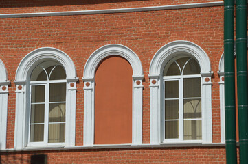 Element of the facade of a red brick building with white arched windows.