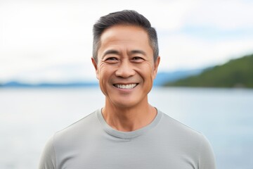 Portrait of a happy asian man in his 50s dressed in a casual t-shirt isolated in serene lakeside view