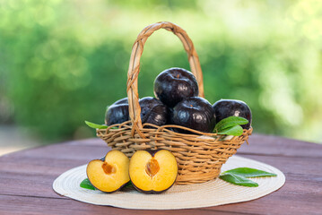 Fresh Black Plum fruit in Bamboo basket on wooden table in garden, Fresh Black Plum with slices on...