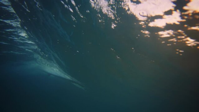 Underwater ocean wave breaking and glowing from sunlight as surfer rides