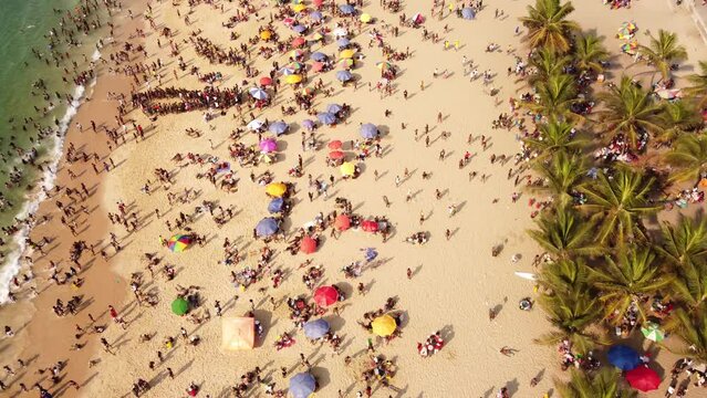 Aerial footage of many of beachgoers with umbrellas and palms on the beach of Ilha de Luanda Island