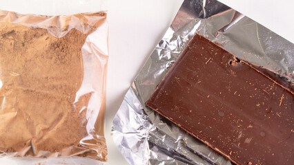 Cocoa and a bar of dark chocolate on a white background. The rise in prices for raw materials for...