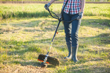 worker mows green grass on the lawn with hand trimmer. lawn care. weed control. Woman with gasoline...