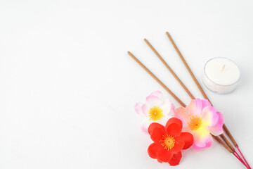 Isolated Empty white background decorated with colorful flowers, red colored incense and round white candle. Concept for Vesak Day and Enlightenment Day. Empty blank copy text space