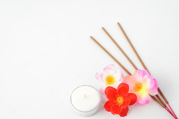 Isolated Empty white background decorated with colorful flowers, red colored incense and round white candle. Concept for Vesak Day and Enlightenment Day. Empty blank copy text space