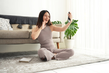 A young Asian woman makes a video call with a shock facial expression, wearing a brown nude shirt...