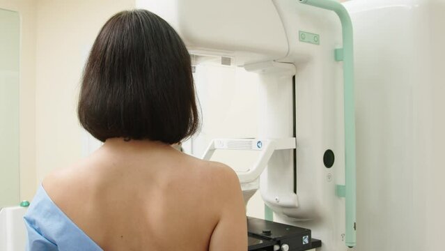 A female doctor in a modern clinic explains the mammography procedure to a topless adult patient undergoing a mammogram. A healthy woman is engaged in cancer prevention in a hospital ward.