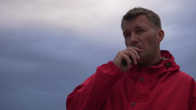 Close-up, a brunette man smoking an electronic cigarette against the background of a cloudy and dark sky