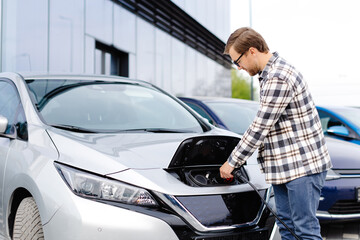 Young man plugging charging cable into the car socket. Electric car charging concept