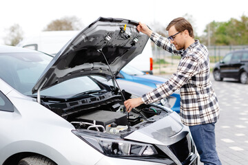 Young man checking under the hood of his car to figure out what the problem is.