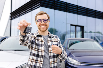 Emotional guy holding key in hand and smiling at camera. Man showing key from his new electric car....