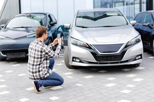 Man customer taking photo to mobile phone chooses auto and wants to buy new car in showroom