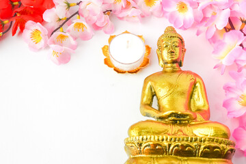 A golden statue of a Buddhist figure meditating decorate with colorful flowers and round white...