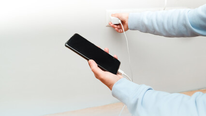 Female holding phone while charging from wall outlet. Woman using charging power to smart phone.