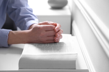Religion. Christian woman praying over Bible indoors, closeup
