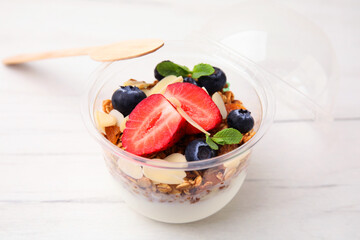 Tasty granola with berries, almond flakes and yogurt in plastic cup on white wooden table, closeup