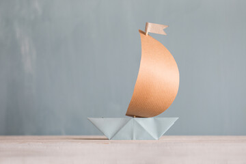 Segelboot aus Papier mit Mast aus Holz auf blauen Hintergrund - geeignet für Themen wie Aufbruch,...