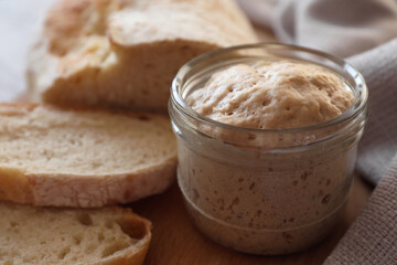 Sourdough starter in glass jar and bread on table, closeup
