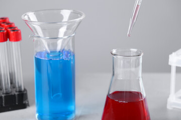 Dripping liquid from pipette into flask on grey background, closeup