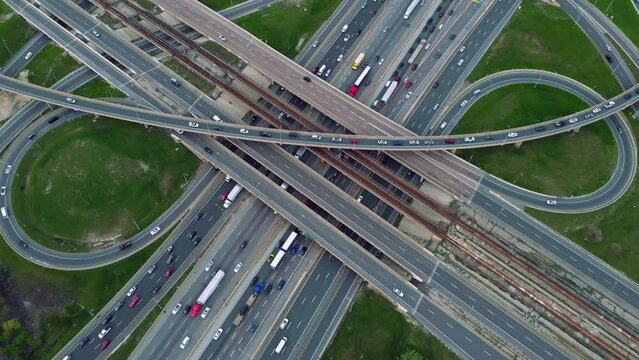 Sprawling highway networks alive with movement, cars navigate concrete sprawl in aerial view. Multi-tiered urban roadways brim with commuters, drone video reveals organized chaos in motion.