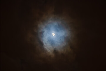 The Moon is surrounded by colorful glowing clouds in the dark night sky. Night sky scene