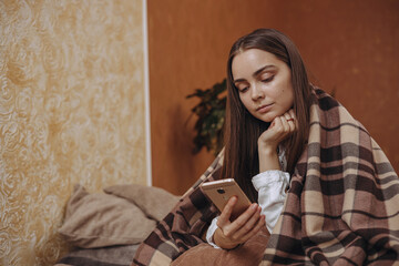 Woman wrapped in plaid using smartphone and relaxing at home 