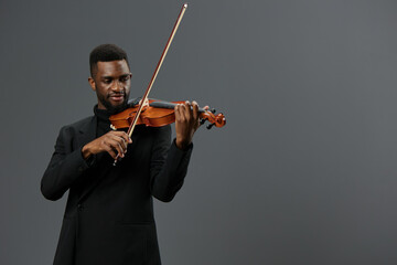 Talented African American Man in Black Suit Playing Violin on Gray Background