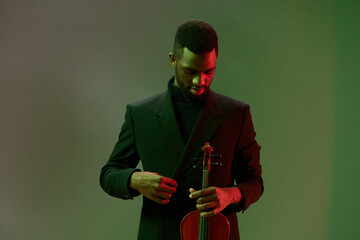 Man in black suit playing a violin in front of a glowing green background, creating an elegant and...