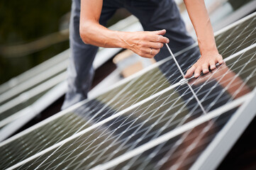 Man worker mounting photovoltaic solar moduls on roof of house. Close up of electrician installing...