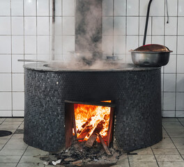 large cauldron on a wood stove with fire for cooking traditional Uzbek pilaf in a restaurant in...