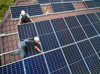 Men technicians mounting photovoltaic solar moduls on roof of house. Workers in helmets installing...