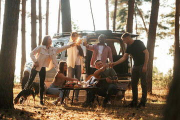 Obraz premium Making cheers with beer bottles. Group of friends are having fun together in the forest