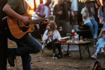 Guy is playing acoustic guitar. Group of friends are having fun together in the forest