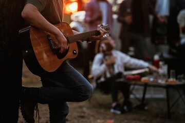 Guy is playing acoustic guitar. Group of friends are having fun together in the forest
