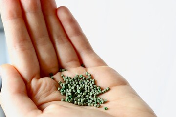 Kunststoffgranulat (grün) in einer Hand vor weißem Hintergrund Closeup, Kunststoff als Rohstoff...