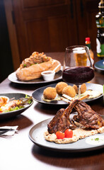 dinner at a steakhouse with rack of lamb with mashed potatoes and cherry tomatoes and glass of red wine and craft beers and blurred background