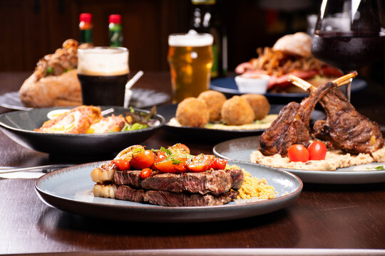 dinner banquet table in a steakhouse with sirloin steak and farofa in focus and rack of lamb out of focus and other dishes