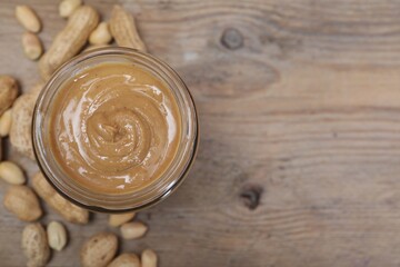 Tasty peanut nut paste in jar on wooden table, top view. Space for text