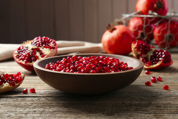 Ripe juicy pomegranate grains in bowl on wooden table