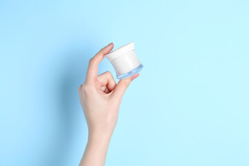 Woman holding jar of cream on light blue background, closeup. Space for text