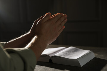 Religion. Christian man praying over Bible at table, closeup