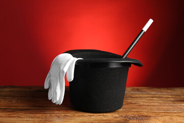 Magician's hat, gloves and wand on wooden table against red background