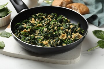 Tasty spinach dip with eggs in dish served on white table, closeup