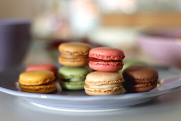 Plate of pastel macarons, cookies and chocolate, cup of tea of coffee, glass of bubble water, various berries, books and accessories on the table. Selective focus, pastel colors.