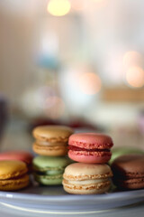 Plate of pastel macarons, cookies and chocolate, cup of tea of coffee, glass of bubble water, various berries, books and accessories on the table. Selective focus, pastel colors.