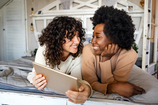 Happy multiethnic diverse homosexual lesbian gay couple looking at digital tablet together at home