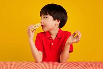 Korean boy in red polo shirt sitting at table and eating instant noodles against yellow background. Fast made dinner. Concept of food, childhood, emotions, meal, menu, pop art