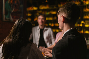 Young couple with friends enjoys night in modern bar backside view. Man and woman meet at double...